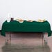 A table with a Hunter Green Creative Converting plastic tablecloth and food on it.