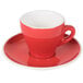 A red CAC Venice espresso cup on a saucer with a white surface.