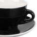 A close up of a black CAC Venice coffee cup and white saucer.