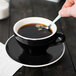 A hand holding a CAC black cup of coffee with a spoon.