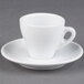 A close-up of a CAC white espresso cup and saucer on a gray surface.