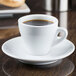A white CAC Venice espresso cup full of brown liquid on a saucer.