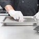 A person in gloves using a Vollrath stainless steel tray on a counter.