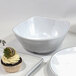 A white melamine bowl with a black border with a cupcake with a strawberry on a plate.
