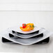 A stack of white Elite Global Solutions melamine plates with a yellow and red pepper on top.