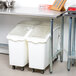 An Advance Tabco stainless steel open base work table with white plastic containers on the shelves.