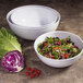 A white Elite Global Solutions melamine bowl filled with salad with tomatoes and carrots on a table.