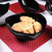 A close-up of a black Elite Global Solutions triangular bowl filled with croissants on a red place mat.