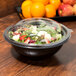 A Fineline black plastic bowl filled with salad on a table.