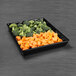 A black tray with broccoli and carrots on a table in a salad bar.