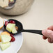 A hand holding a black Elite Global Solutions spoon with fruit on a plate.