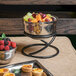 A bowl of fruit on an Elite Global Solutions reversible round steel stand next to a tray of fruit.