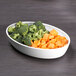 A white oval melamine bowl filled with broccoli and carrots on a table.