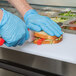 A person wearing blue gloves cutting a sandwich on a counter with an Arctic Air 2 Door Mega Top Refrigerated Sandwich Prep Table.
