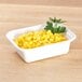 A white Pactiv rectangular microwavable container with yellow corn and parsley on a wooden surface.