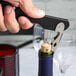 A person using a Franmara Boomerang Waiter's Corkscrew with a black handle to open a wine bottle.