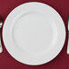A white 10 Strawberry Street Royal White porcelain charger plate with a fork and knife on a red surface.