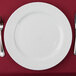 A white 10 Strawberry Street Wicker porcelain charger plate with a fork and knife on a red tablecloth.