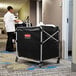 A man in a white coat standing in a hallway with a Rubbermaid 8 Bushel Laundry Cart.