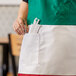 A person wearing a green and white Intedge Italian bib apron with a pocket full of toothpicks.