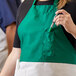 A person holding a pen in a green Intedge Italian Poly-Cotton bib apron.