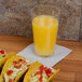 A GET customizable plastic mixing glass filled with orange juice sits on a table with tacos.