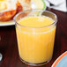 A GET clear plastic short tumbler filled with orange juice on a table.
