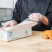 A person wearing plastic gloves using an LK Packaging plastic resealable sandwich bag to put a sandwich in a white box.