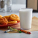 A clear plastic GET pebbled tumbler filled with milk on a table with chicken nuggets.