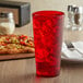 A red GET plastic tumbler filled with red liquid and ice on a table with a pizza.