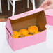 A hand holding a pink cake box with cupcakes inside.