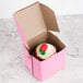 A pink cupcake in a bakery box with a strawberry on top.