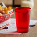 A close up of a red cup with a straw in it on a table with a red basket of food