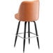 A close-up of a Lancaster Table & Seating caramel brown vinyl bar stool with a swivel bucket seat on a black base.