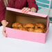 A woman holding a pink bakery box of croissants.