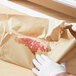 A person in gloves uses Bagcraft Packaging EcoCraft Freezer Paper to wrap a piece of meat in a brown paper bag.