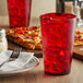 A close up of a red GET plastic tumbler filled with red liquid and ice on a table with a pizza.