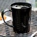 A close-up of a black Carlisle Tritan mug on a table with a spoon and a pastry.