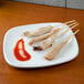 Grilled chicken skewers with sauce on a Tuxton eggshell white square plate.