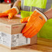 A person wearing Cordova orange freezer gloves holding a box.
