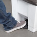 A person's foot stepping on a white Rubbermaid rectangular step-on trash can pedal.