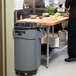 A man standing in a school kitchen with a Rubbermaid grey trash can.