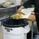 A person cutting food on a counter and throwing the scraps into a Rubbermaid 44 gallon white round trash can.