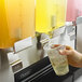 A hand pouring liquid from an Omega OSD30 Triple Refrigerated Beverage Dispenser into a plastic cup.