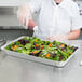 A person pouring sauce into a Western Plastics foil tray of salad.