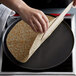 A person using a Chasseur cast iron crepe pan and wooden spatula to make a pancake.