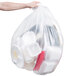 A hand holding a Berry clear plastic trash bag full of plastic containers.