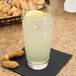 A Libbey cooler glass of lemonade with ice and a lemon slice, with peanuts in the background.