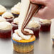 A hand using an Ateco dual-color pastry bag to put chocolate frosting on a cupcake with white frosting and chocolate swirls.