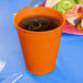 A Sunkissed Orange plastic cup filled with liquid on a blue table.